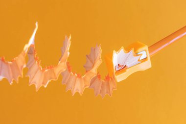 Turuncu arka planda, kırtasiye kaleminde talaş bulunan turuncu ahşap kalem. Monokrom görüntüsü. Yaratıcı çizim konsepti, yaratıcılık, öğrenme. Minimalizm, boşluğu kopyala.