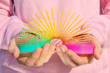 Pembe bir kazağın arka planında elleri olan oyuncak plastik gökkuşağı. 90 'larda popüler olan oyun ve numaralar için renkli spiral. Minimalizm. Oyuncaklar, çocukluk kavramı. parlaklık.