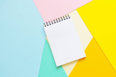 Çok renkli kağıtların üzerinde boş beyaz kağıtlar olan sarmal bir defter. Ofis, okul, yaratıcılık, öğrenme kavramı. Üst görüş, düz alan, kopyalama alanı, minimalizm. Pembe, mavi, turuncu ve sarı gölgeler.