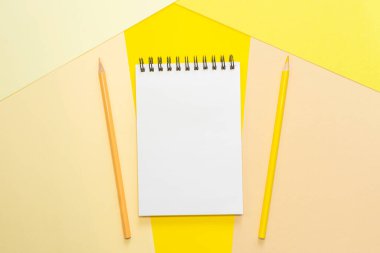 Beyaz sayfalı, sarmal defter ve renkli kalemler. Çok renkli kağıtlar. Ofis, okul, yaratıcılık, öğrenme kavramı. Üst görüş, düz alan, kopyalama alanı, minimalizm. Sarı gölgeler.