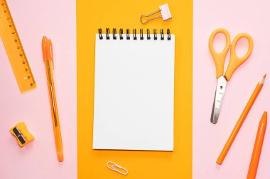 Boş beyaz sayfalı sarmal not defteri, turuncu makas, cetvel, kalem, renkli arka planlarda keskinleştirici kalem. Ofis, okul, yaratıcılık, öğrenme Üst görünüm, düz görünüm, kopyalama alanı, minimalizm
