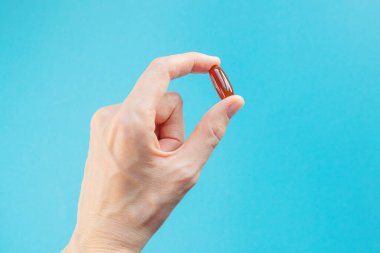 Kahverengi lesithin kapsülü mavi arka planda bir kadının elinde. Vitamin konsepti, beslenme takviyeleri.