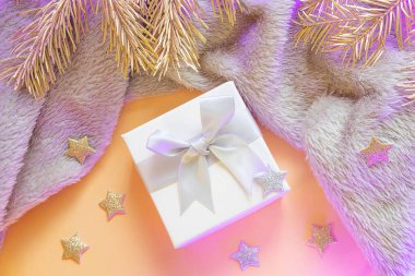 Yakından fiyonklu küçük kare bir hediye. Yakınlarda ekoseli, altın bir Noel ağacı dalları ve şenlikli yıldız süslemeleri var. Yeni yıl konsepti, Noel, ev konforu. Neon ışığı.