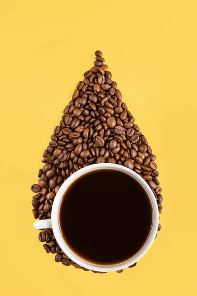 White cup and coffee beans in the form of a drop on a yellow background. Creative concept for coffee shops. Top view, copy space, minimalism, conceptual flat lay.