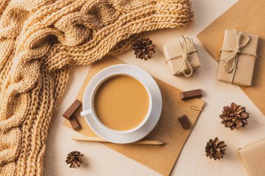 Konforlu ev yatağı: Kahveli beyaz bardak, kalın örgü eşarp, kalemli defter, hediyeler. Gelecek kış, Noel arifesi ve yeni yıl konsepti. Sıcak gölgeler, yakın plan..