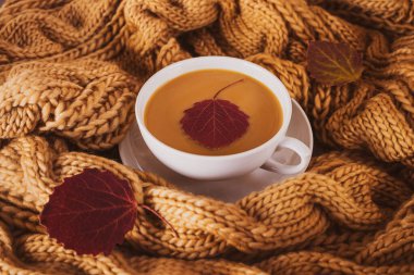 Samimi bir sonbahar evi, beyaz fincanda kahve ve tıknaz örgü eşarp. Kış konsepti Sıcak gölgeler, yakın plan..