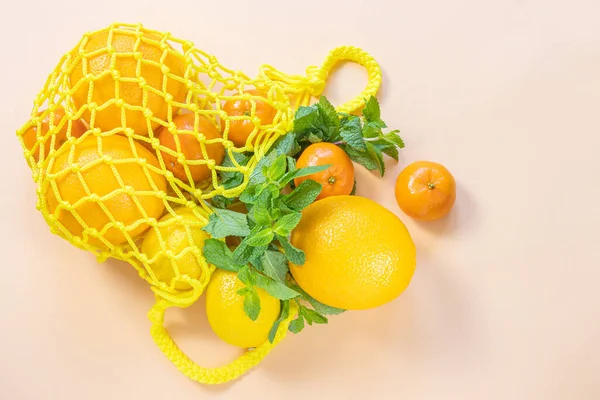 Oranges, tangerines, lemons in a yellow string bag. Citruses, vitamin C. Sustainability, zero waste, plastic free concept, vegetarianism, healthy food. Top view.