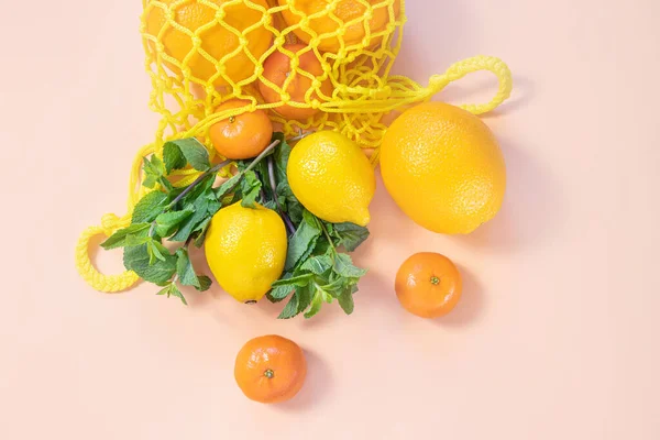 Oranges, tangerines, lemons in a yellow string bag. Citruses, vitamin C. Sustainability, zero waste, plastic free concept, vegetarianism, healthy food. Top view.