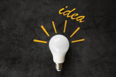 Koyu arkaplanda bir ampul, renkli kağıt ışınları ve yazıt fikri etrafında. Yaratıcılık kavramı.