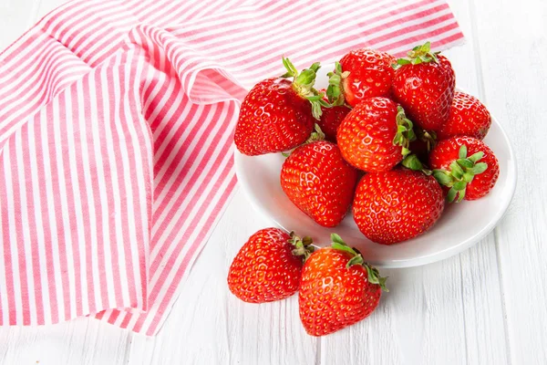 Verse rijpe aardbeien op een plaat. Witte houten tafel, servet in rode en witte strepen. — Stockfoto