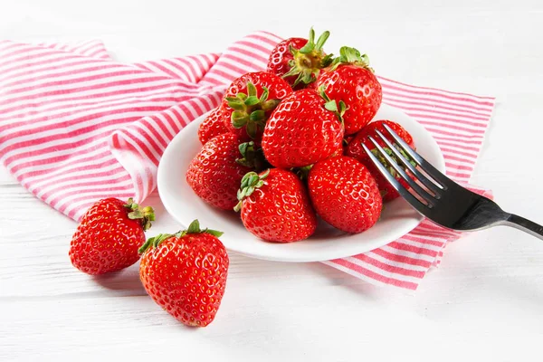 Verse rijpe aardbeien op een plaat. Witte houten tafel, servet in rode en witte strepen. — Stockfoto