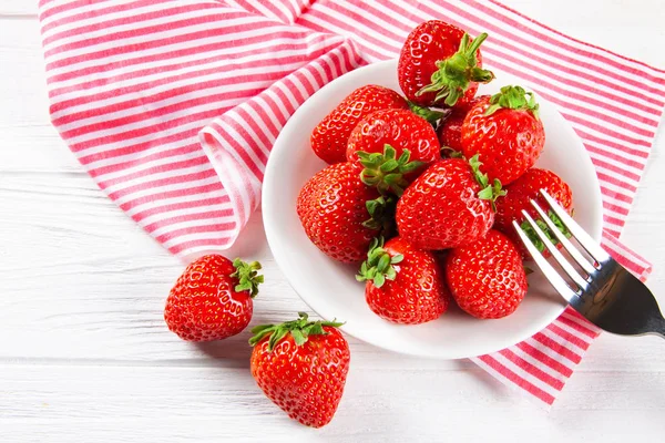 Verse rijpe aardbeien op een plaat. Witte houten tafel, servet in rode en witte strepen. — Stockfoto