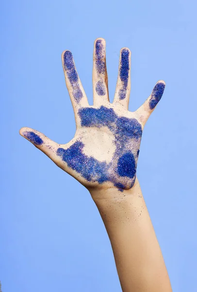 Öppen handflata beströs med blå metallic spangles. Handen lyfts upp — Stockfoto