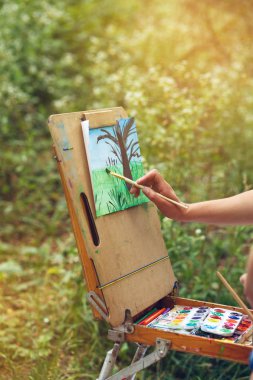 Doğada bir şövale üzerinde çizim. Sanatçı suluboya ağaçları çizer