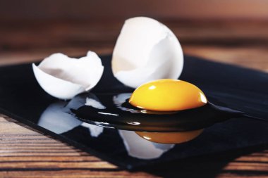 Ahşap masa üzerinde siyah kesme Kurulu üzerinde çiğ kırık yumurta ve kabuk.