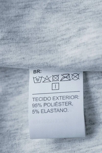 Clothing care label. Close-up tag on a knitwear. Light gray fabric. Vertical photography