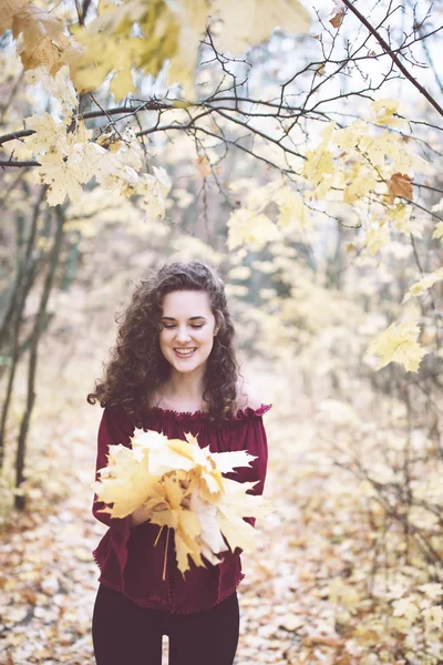 秋の公園カエデの葉を押しながら笑顔で栗色の上部の暗い髪の中で美しい少女 — ストック写真