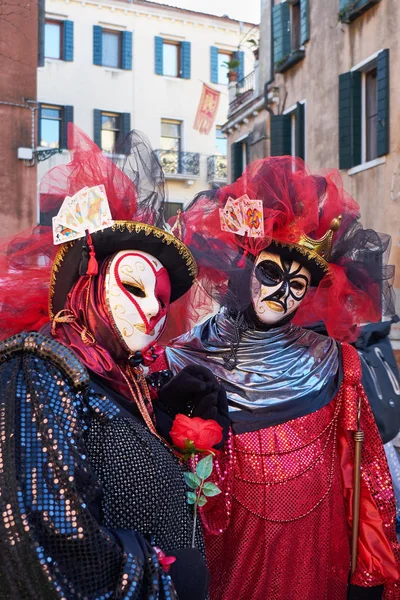 Couple in Queen of Hearts and King of Clubs black and red costumes and white masks on the street during the Carnival in Venice, Italy