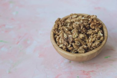 Ceviz taneleri, pembe bir arka plan, sağlıklı beslenme vegan gıda yakın, seçici odak kavramı üzerinde ahşap bir kase içinde soyulmuş fındık.