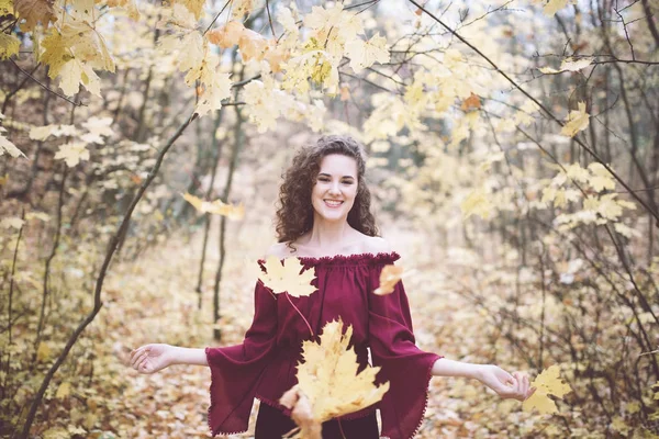 Happy girl in an atumn park throwing maple leaves — Stock Photo, Image