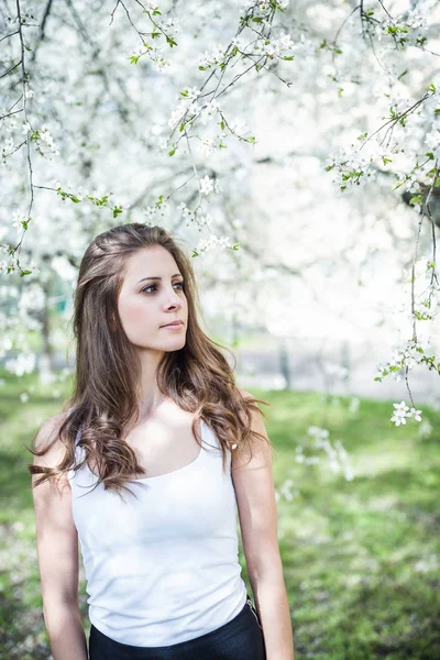 Mladá žena s dlouhými vlasy v bílém tričku pod kvetoucími stromy — Stock fotografie