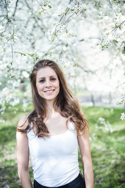 Joyeux cheveux longs jeune femme dans un t-shirt blanc sous les arbres en fleurs — Photo