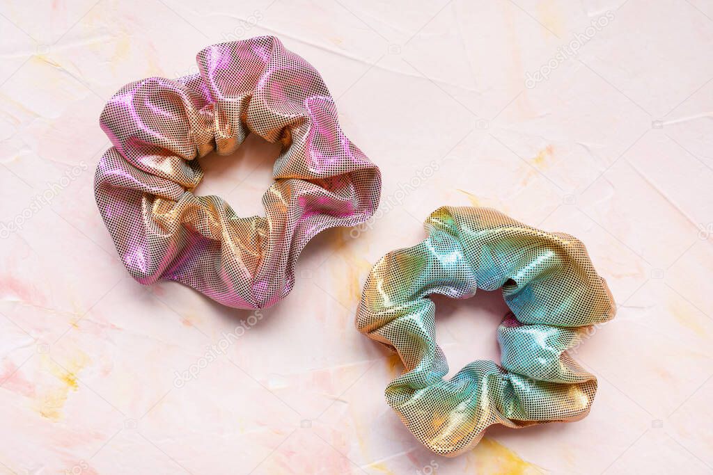 Two trendy holographic scrunchies on pink background