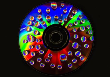 Bir kompakt disk yüzeyi güzel bir yansıması ile çok renkli bir yüzey üzerinde su damlacıkları closeup.