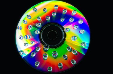 Bir kompakt disk yüzeyi güzel bir yansıması ile çok renkli bir yüzey üzerinde su damlacıkları closeup.