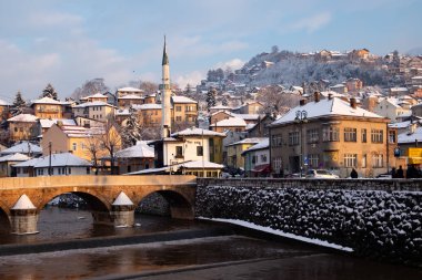 Saraybosna, Bosna-Hersek - 14 Aralık 2016: Kış aylarında Saraybosna'daki Miljacka Nehri üzerindeki Vijecnica köprüsünün manzarası. Bazı yerel halk sağa giden yolda tespit edilebilir.