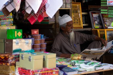 Mumbai, Hindistan - 24 Mart 2019: Yaşlı Müslüman adam Mahim 'deki küçük dükkanında oturmuş gazete okuyor.