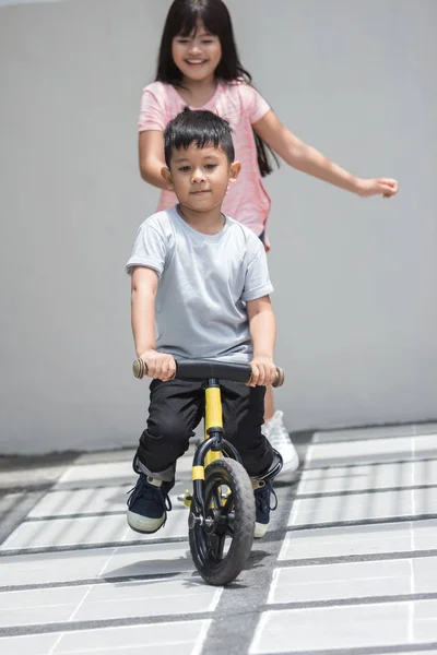 Дети ездят на велосипеде и сестра бежит за ним — стоковое фото