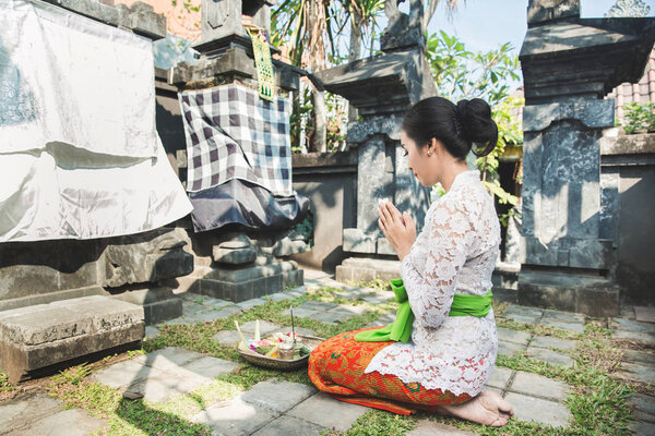 балийская женщина молится в храме на небольших святынях в домах
