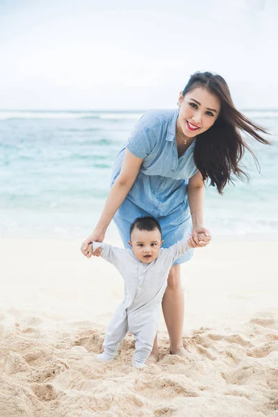 Hermosa madre está enseñando a su hijo camina en la playa — Foto de Stock