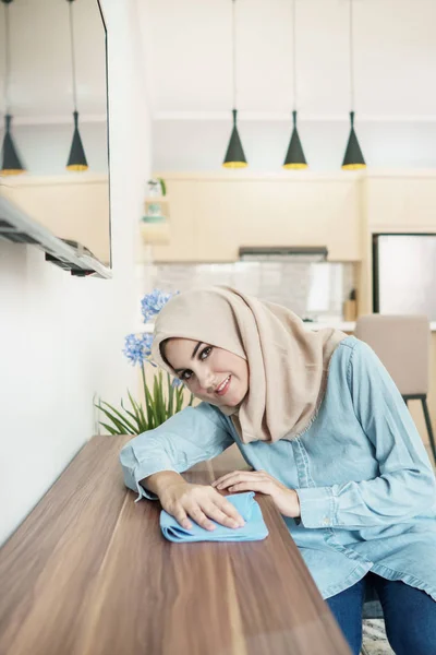 Krásná žena v domácnosti na sobě hidžáb čištění dřevěný stůl v její h — Stock fotografie