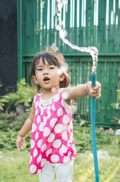 Bela filha brincando de água com tubo de borracha — Fotografia de Stock