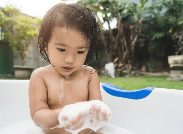 Linda menina tomar um banho e jogar espuma de sabão em um bebê — Fotografia de Stock