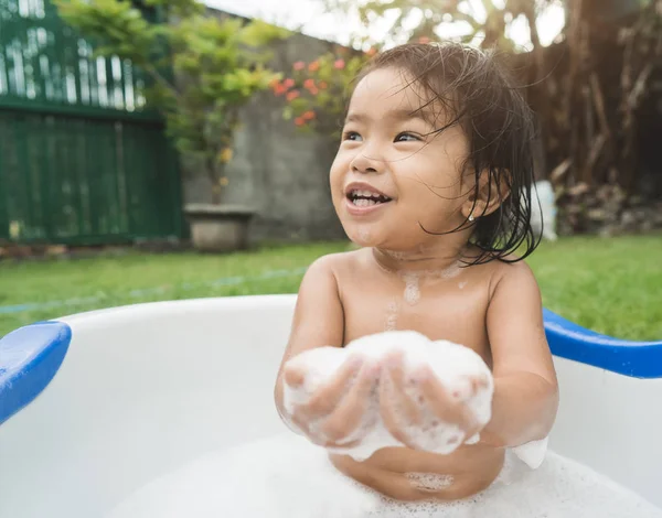 Linda menina tomar um banho e jogar espuma de sabão em um bebê — Fotografia de Stock