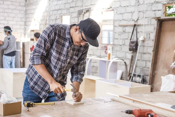 Trabajador en el espacio de trabajo del carpintero instalando clavo usando martillo —  Fotos de Stock