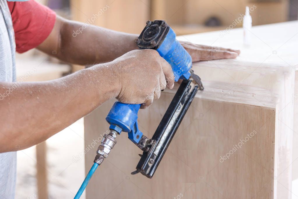 worker at carpenter workspace installing nail using pneumatic na