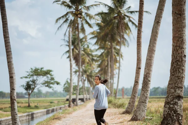 Una donna correva in alberi di cocco laterali, guardando indietro alla macchina fotografica — Foto Stock