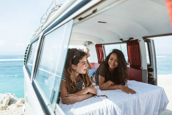 two young woman lay down relax inside of retro van