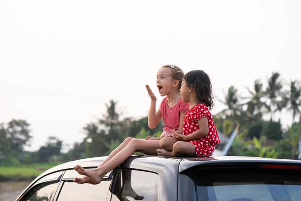 Deux jeunes enfants heureux assis sur le dessus de la voiture et jouer — Photo