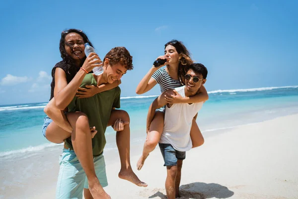 Homens piggybacking mulheres segurando softdrink garrafa — Fotografia de Stock