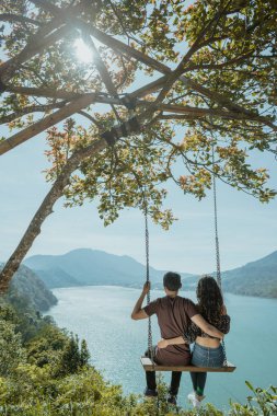 couple enjoying nature from a hill top sitting on a swing clipart