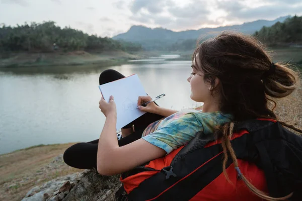 Caucásico mujer solo sentado lado lago y escritura nota —  Fotos de Stock