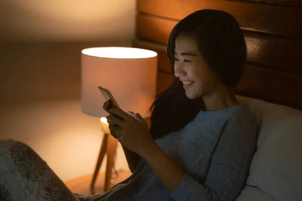 Asiatin mit Smartphone im Bett liegend — Stockfoto