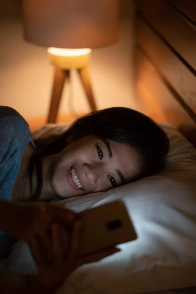 ベッドの上に敷設しながらスマート フォンでアジアの女性 — ストック写真