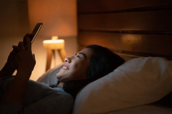 ベッドの上に敷設しながらスマート フォンでアジアの女性 — ストック写真