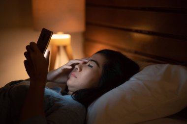 Asyalı kadın Smartphone kullanarak yatakta yatan stres